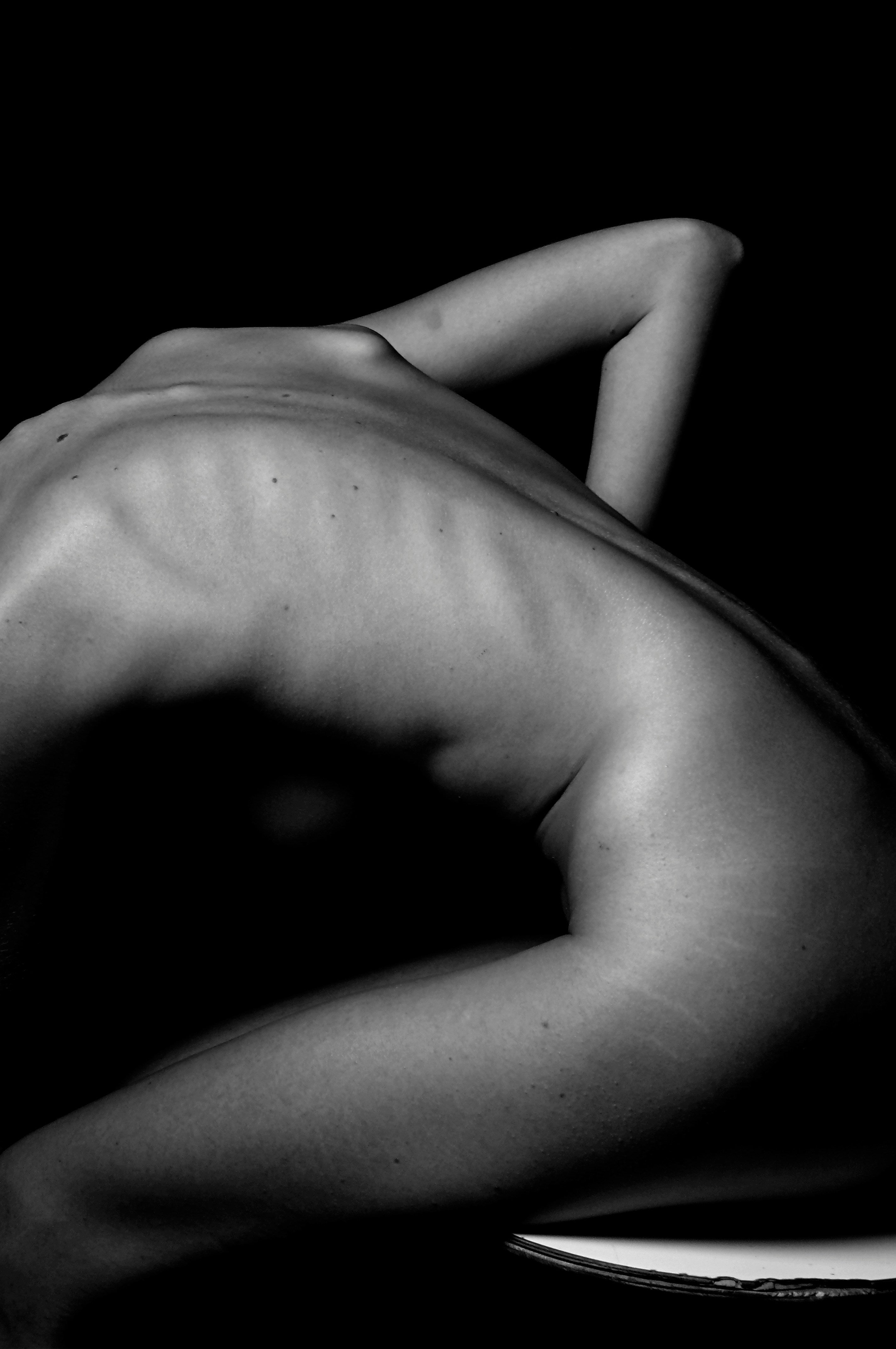 persons nude body arching forward with elbow in the air in side profile. Black and white image
