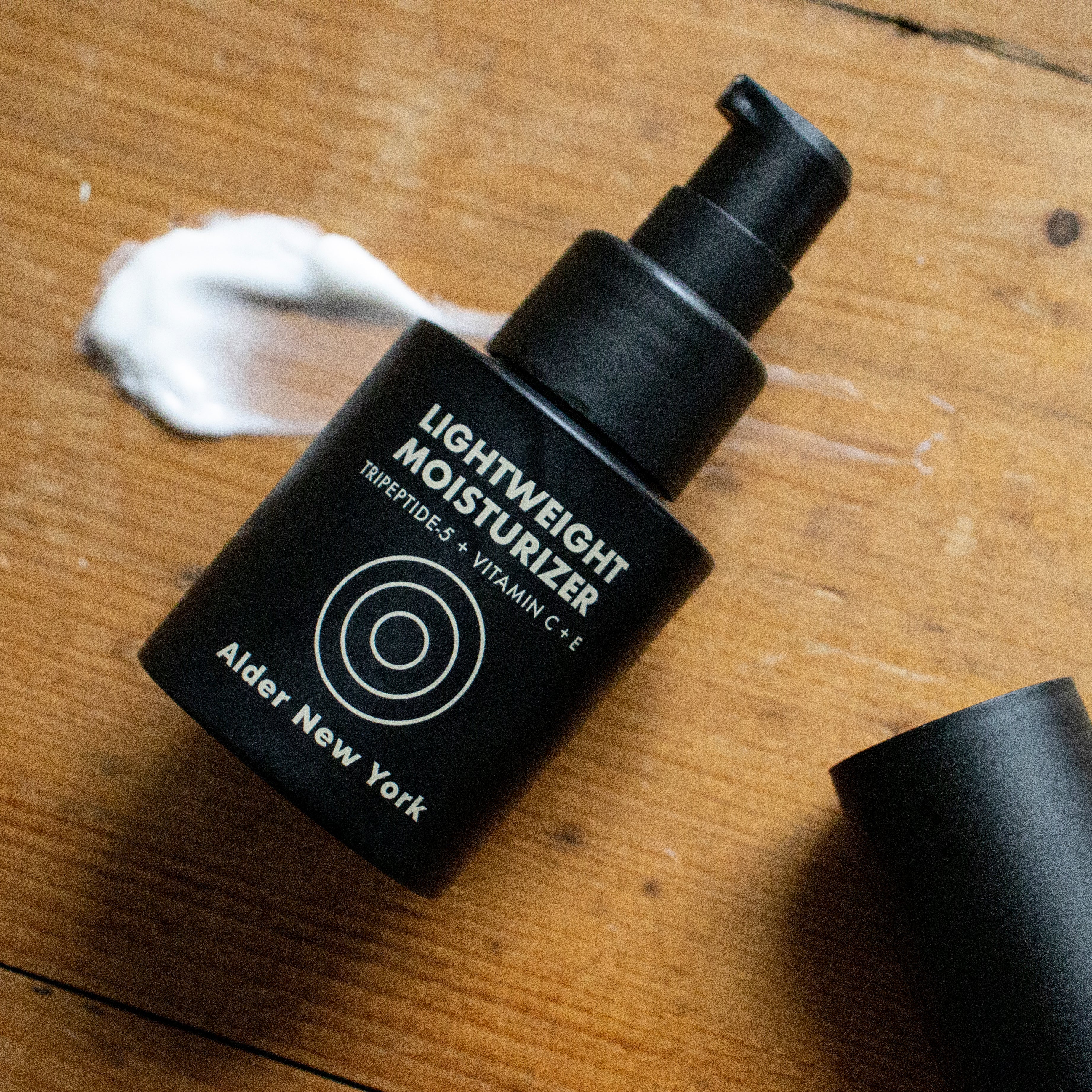 Alder New York's Lightweight Moisturizer bottle on a wood surface with a swipe of cream